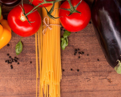 A wide image of a wood counter with an assortment Mediterranean vegetables, pastas and herbs.